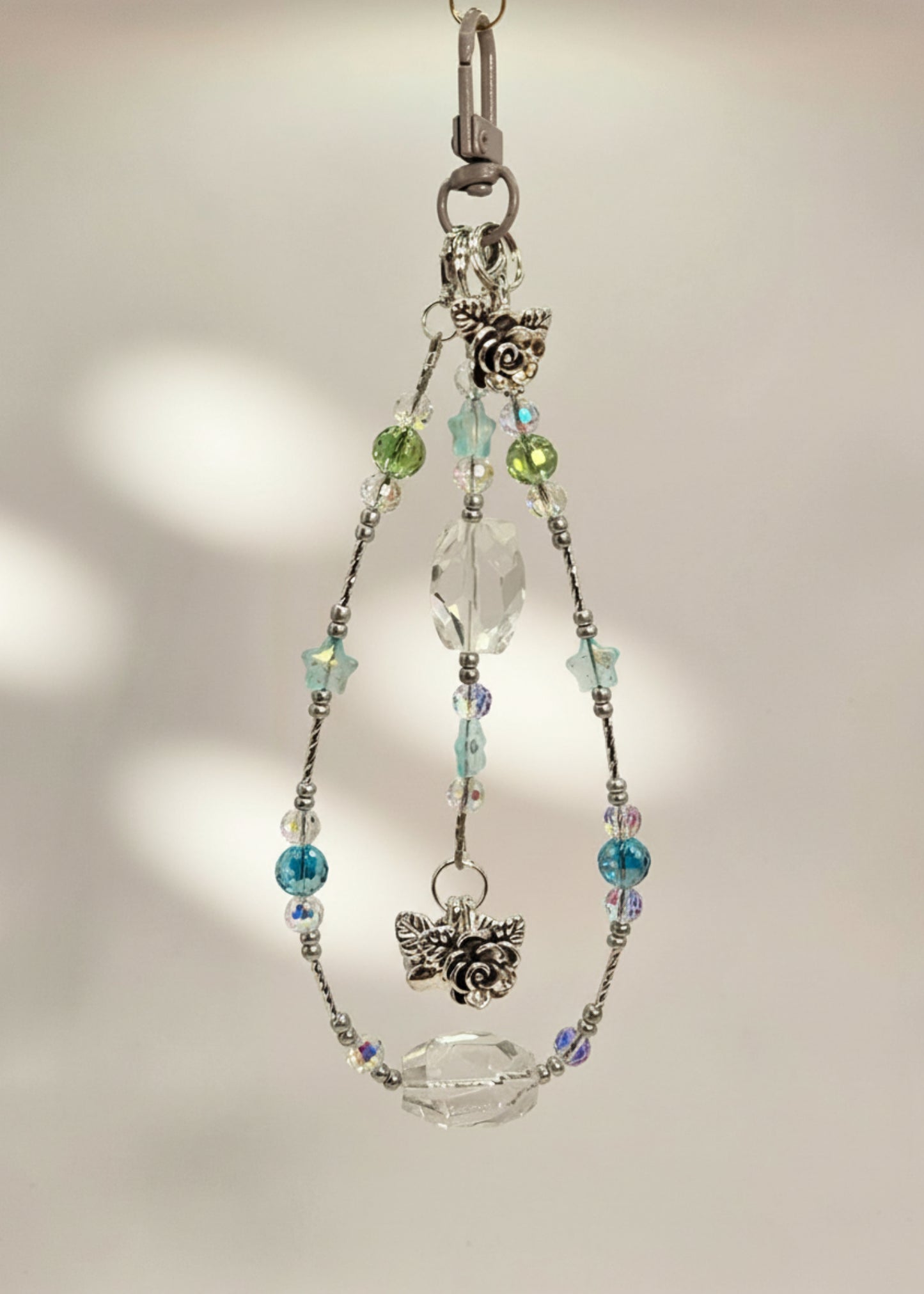 Bag Charm with clear quartz and crystal beads with a silver accent and flower pendants on a beige background