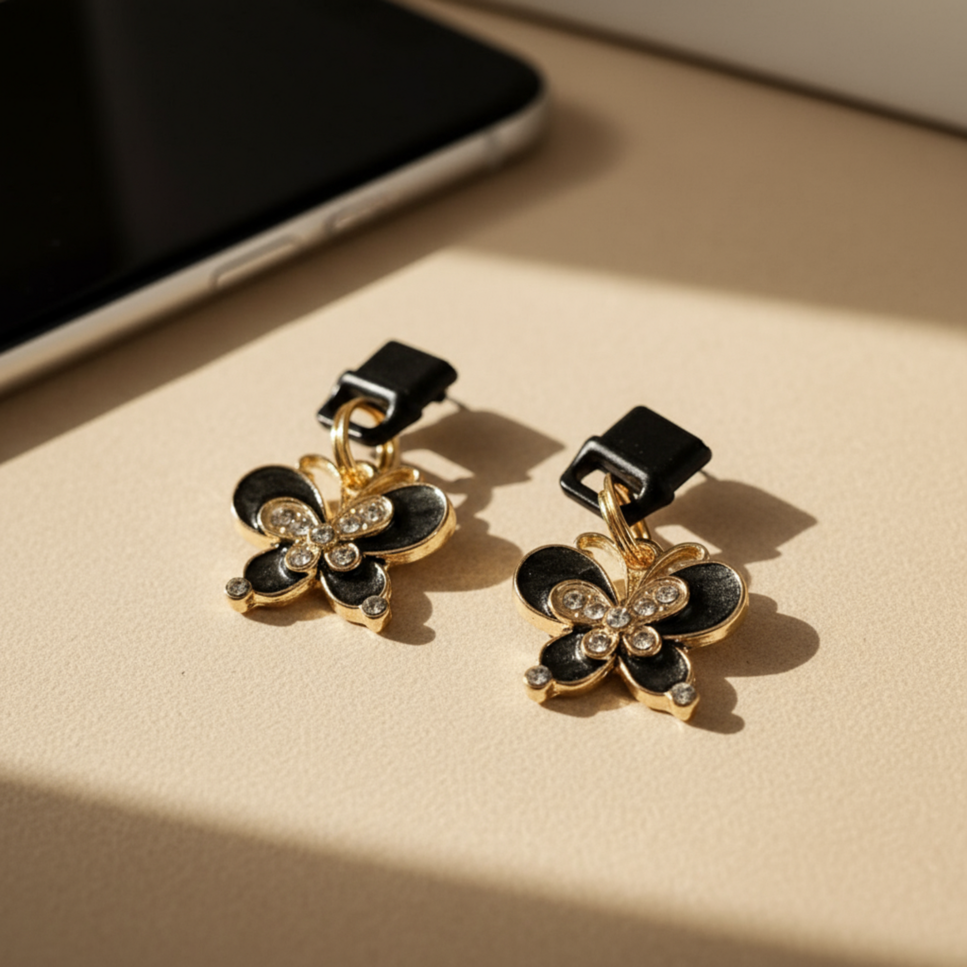 Charging port phone dust cover -Butterfly-shaped charm with black and gold colors on a beige surface