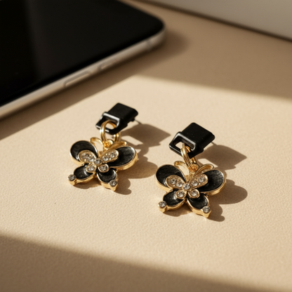 Charging port phone dust cover -Butterfly-shaped charm with black and gold colors on a beige surface