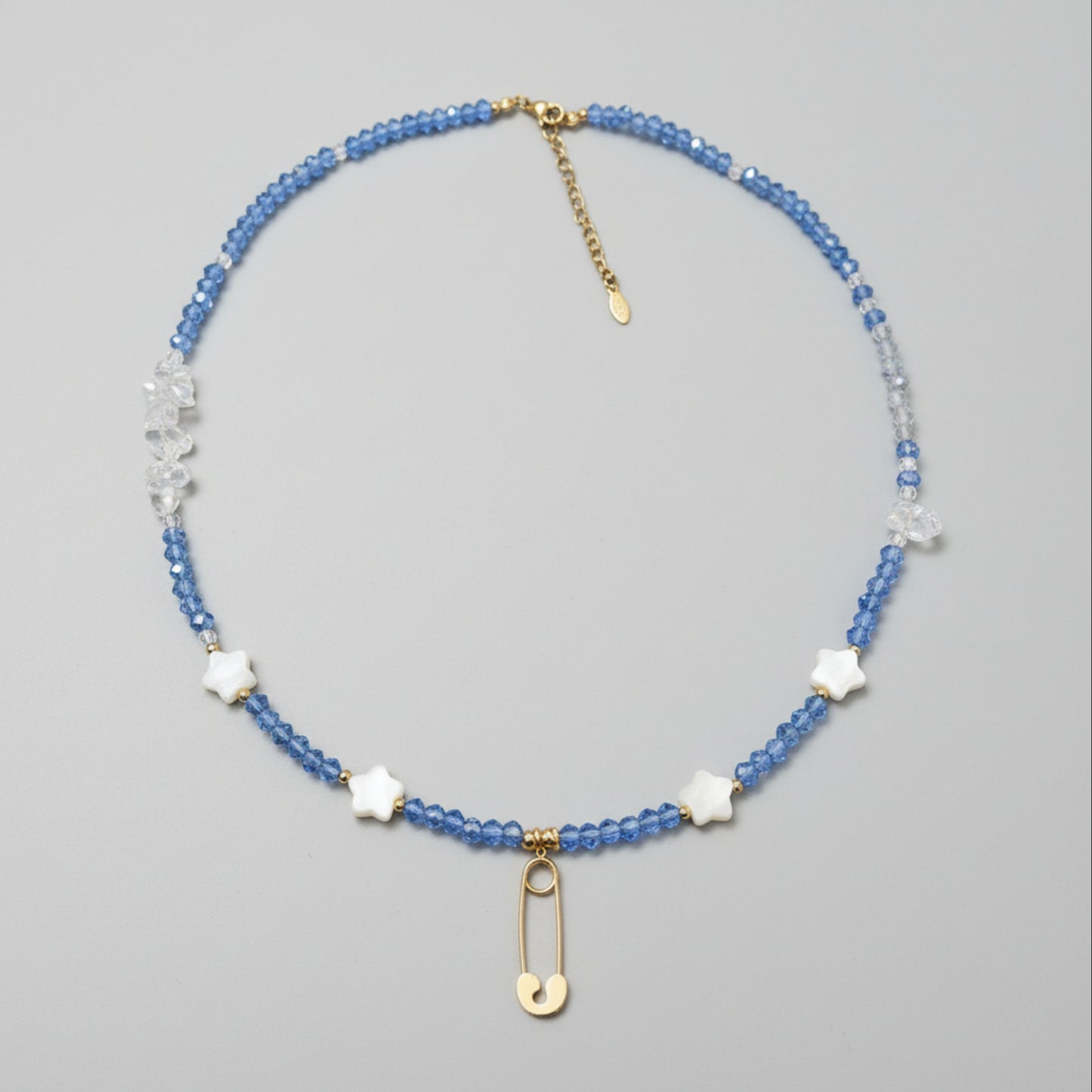 Beaded necklace with blue glass beads, clear quart beads, star shaped shell beads, and gold plated safety pin pendant. 