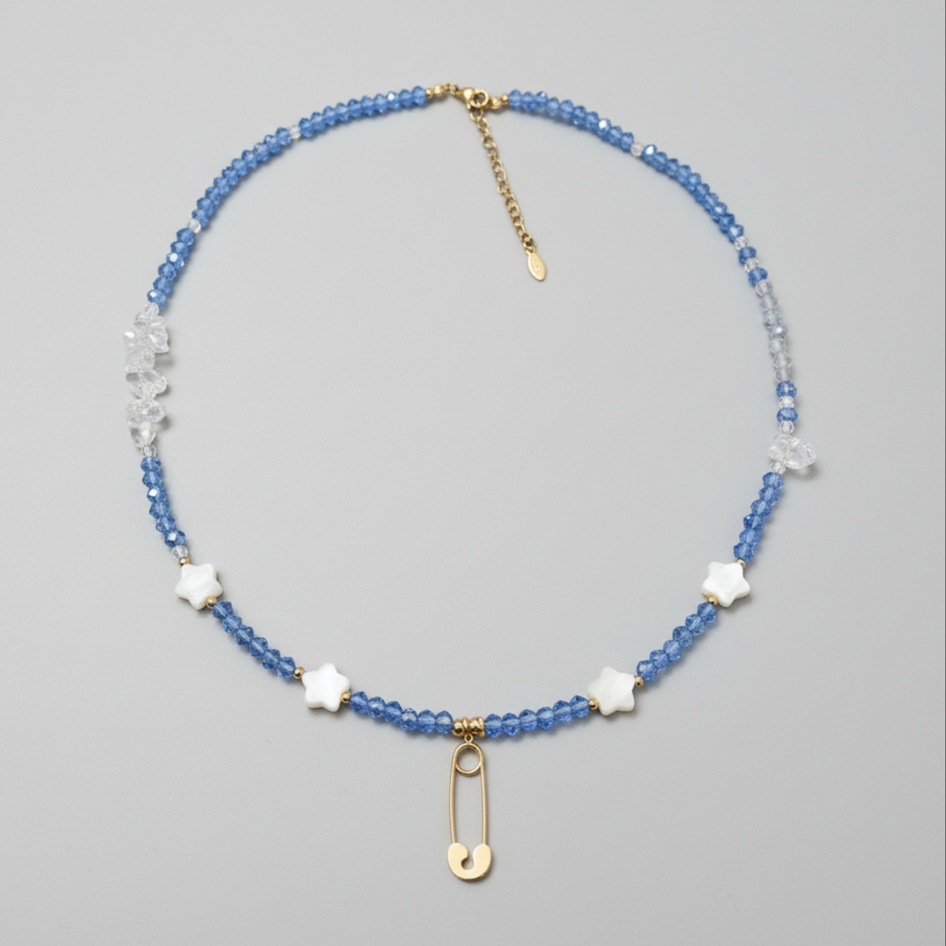 Beaded necklace with blue glass beads, clear quart beads, star shaped shell beads, and gold plated safety pin pendant. 
