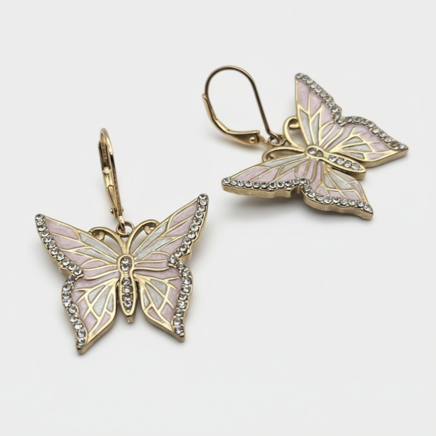 A pair of gold butterfly earrings with metallic finish, featuring butterfly accents in pink and white, and small crystal embellishments.