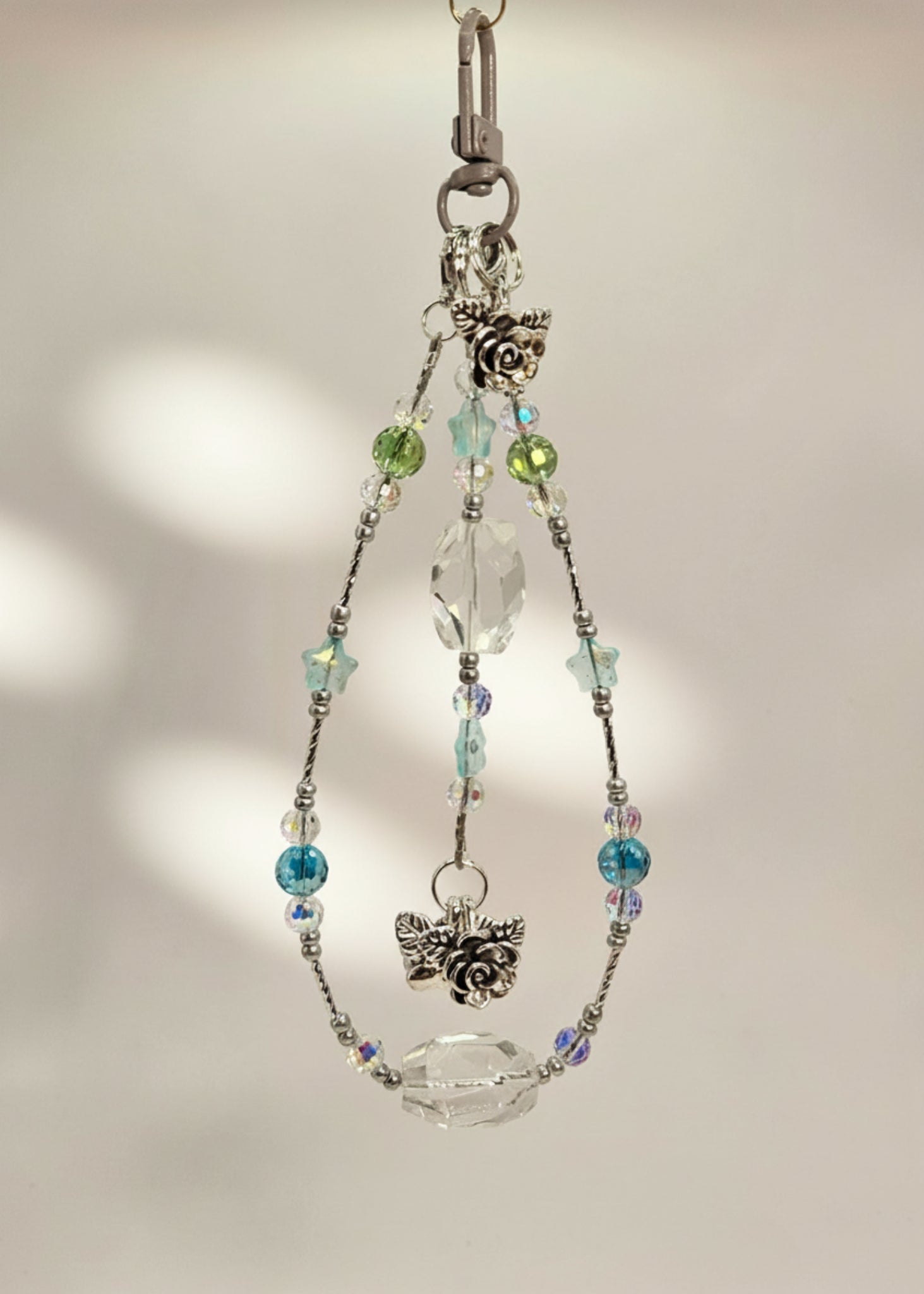 Bag Charm with clear quartz and crystal beads with a silver accent and flower pendants on a beige background