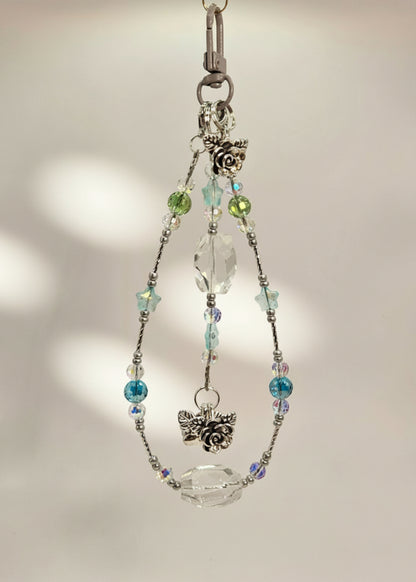 Bag Charm with clear quartz and crystal beads with a silver accent and flower pendants on a beige background