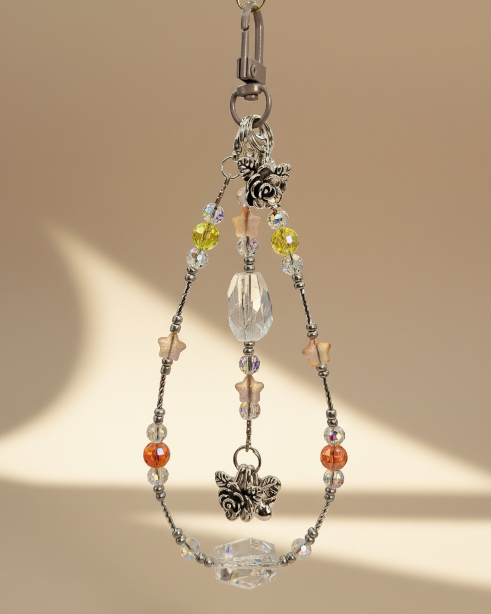 Bag Charm with clear quartz and crystal beads with a silver accent and flower pendants on a beige background. 