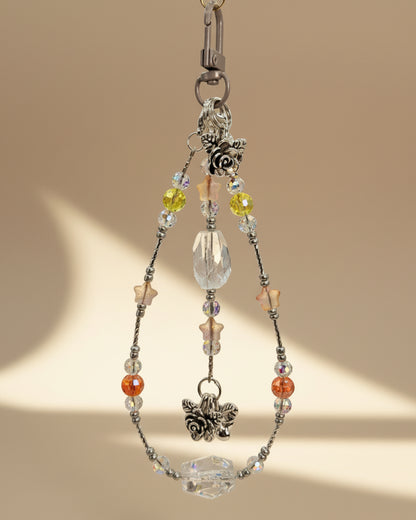 Bag Charm with clear quartz and crystal beads with a silver accent and flower pendants on a beige background. 