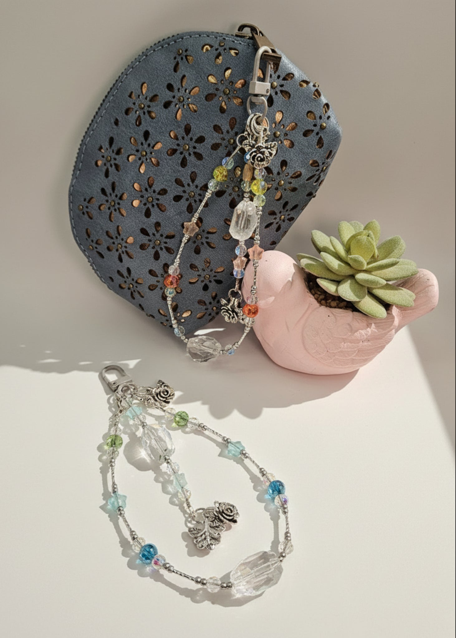Two bag charms on a light surface with a decorative blue pouch and small pink pot with a succulent.